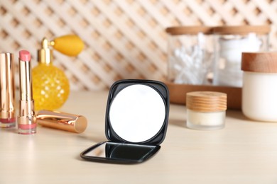 Photo of Stylish pocket mirror and cosmetic products on beige table