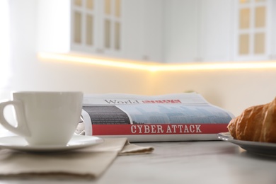 Photo of Newspaper with headline CYBER ATTACK, coffee and croissant on white table indoors