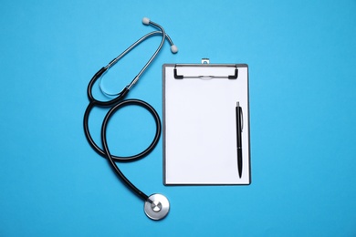 Clipboard, stethoscope and pen on light blue background, flat lay