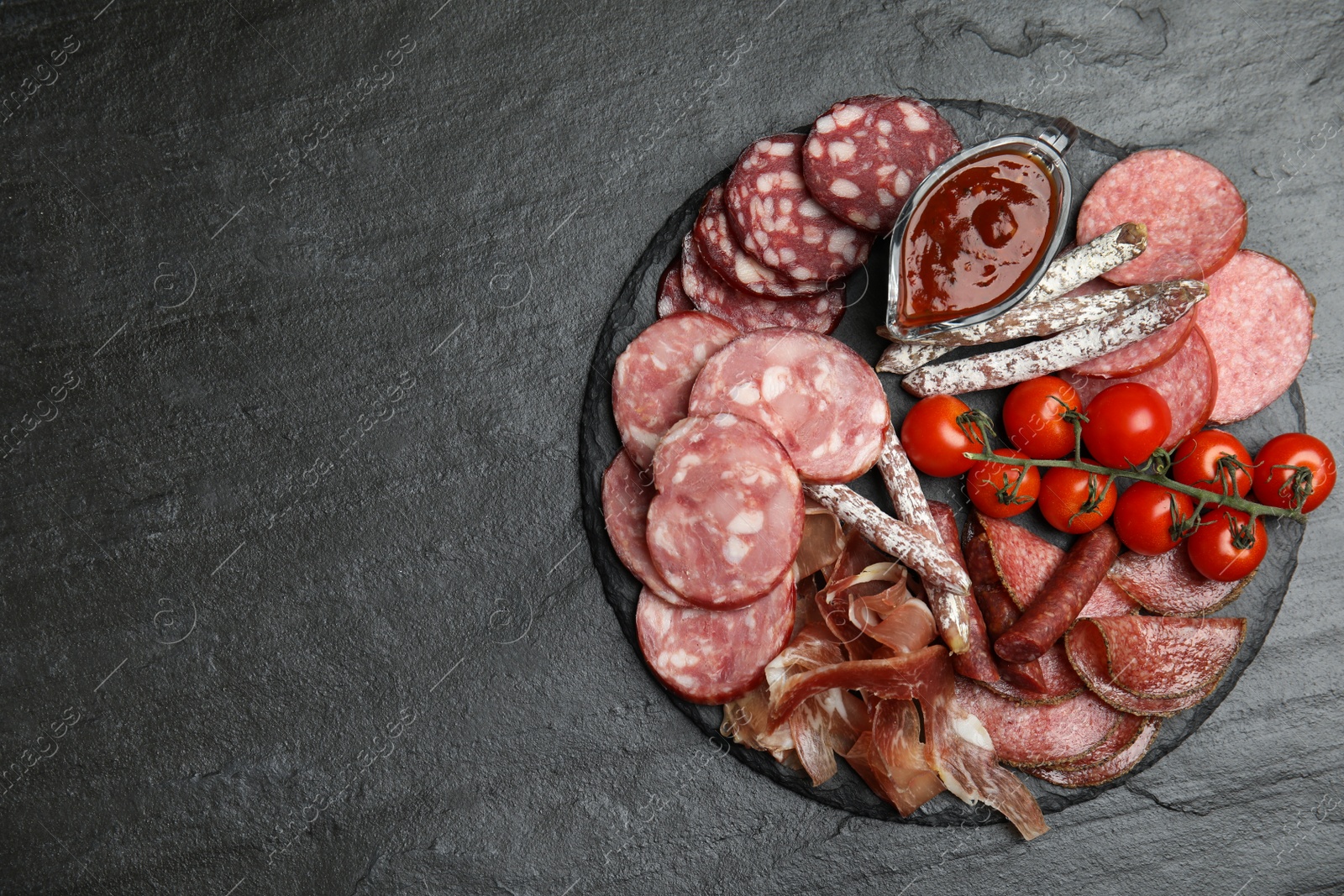 Photo of Different types of sausages with tomatoes served on black table, flat lay