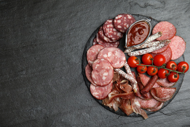 Photo of Different types of sausages with tomatoes served on black table, flat lay