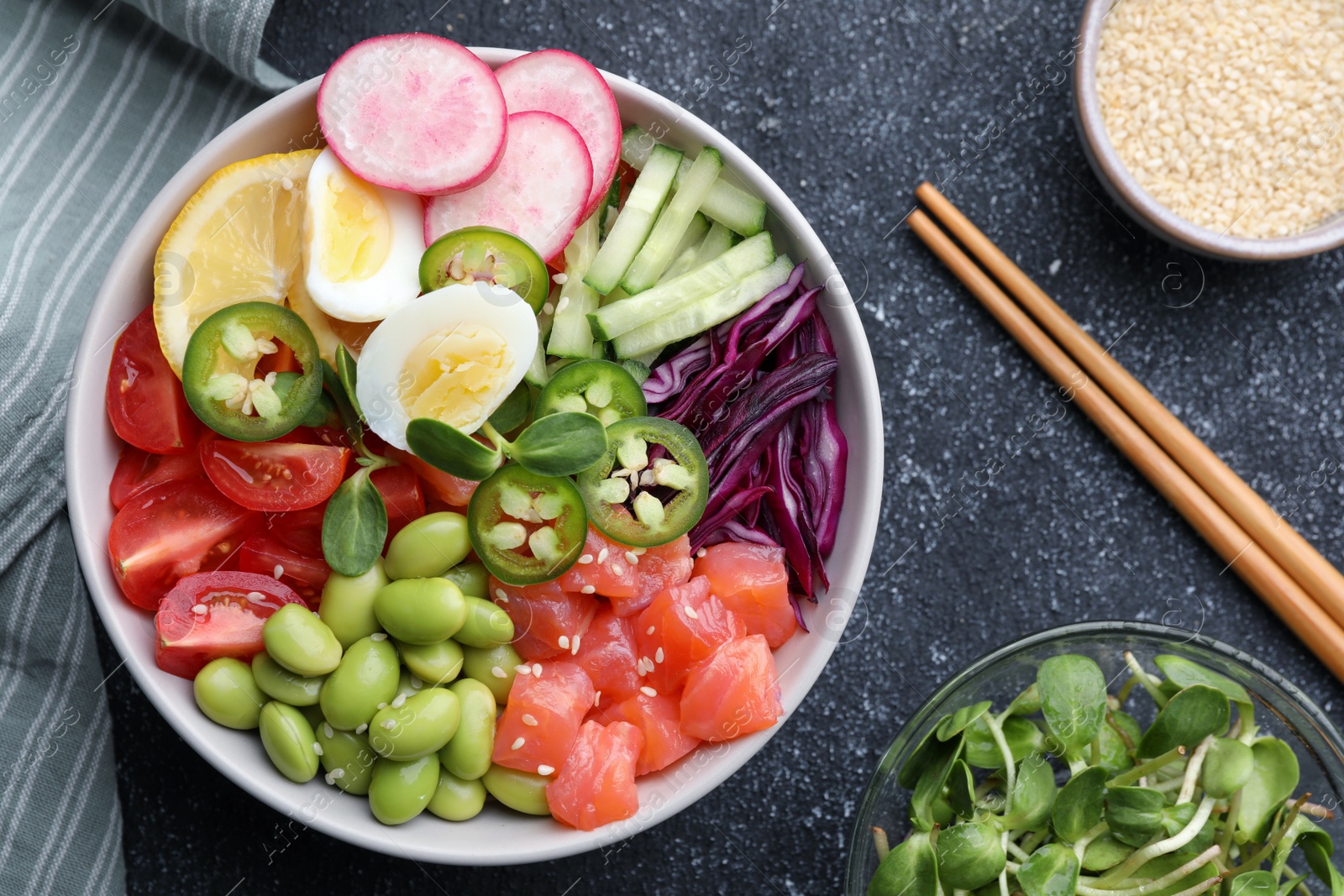 Photo of Poke bowl with salmon, edamame beans and vegetables on black table, flat lay