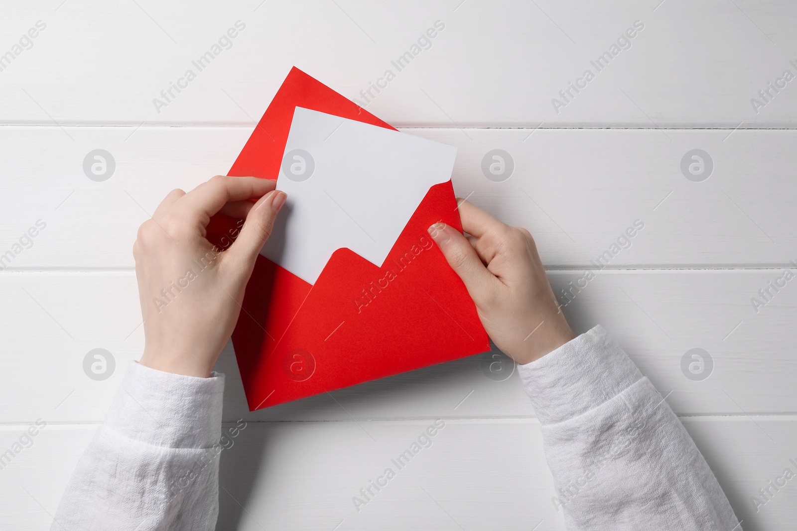 Photo of Woman taking card out of letter envelope at white wooden table, top view