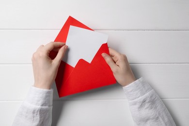 Photo of Woman taking card out of letter envelope at white wooden table, top view