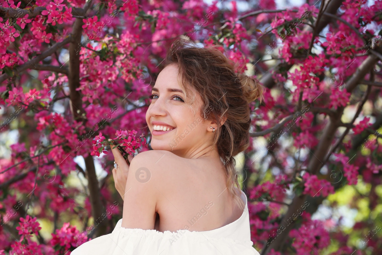 Photo of Attractive young woman posing near blossoming tree on sunny spring day