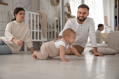 Happy parents watching their baby crawl on floor at home