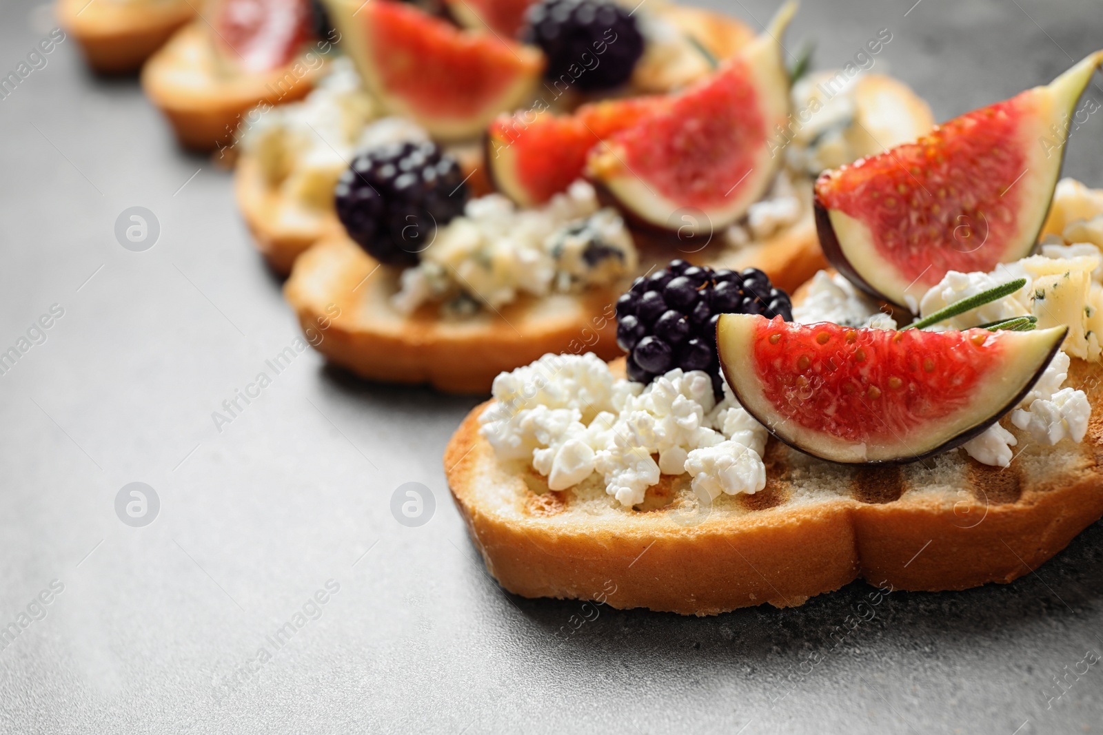 Photo of Bruschettas with cheese, figs and blackberries on grey table, closeup