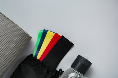 Photo of Set of fitness elastic bands, yoga mat and water bottle on grey background, flat lay. Space for text