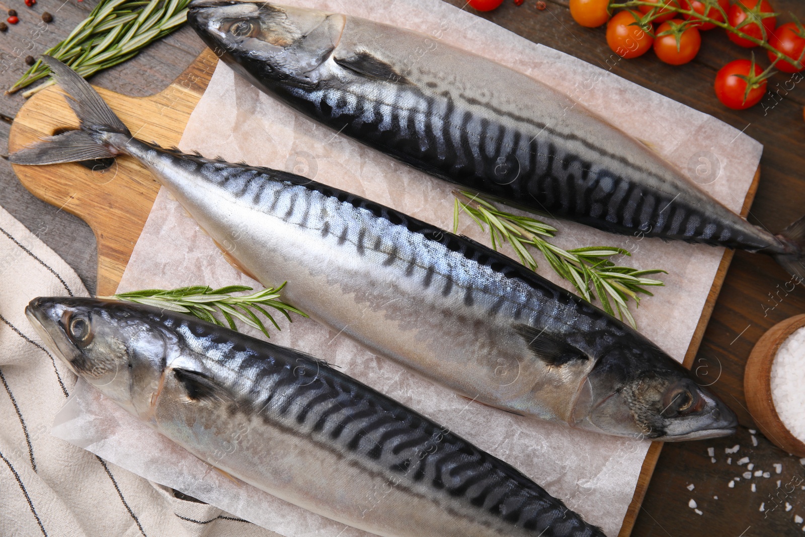 Photo of Raw mackerel, tomatoes and rosemary on wooden table, flat lay