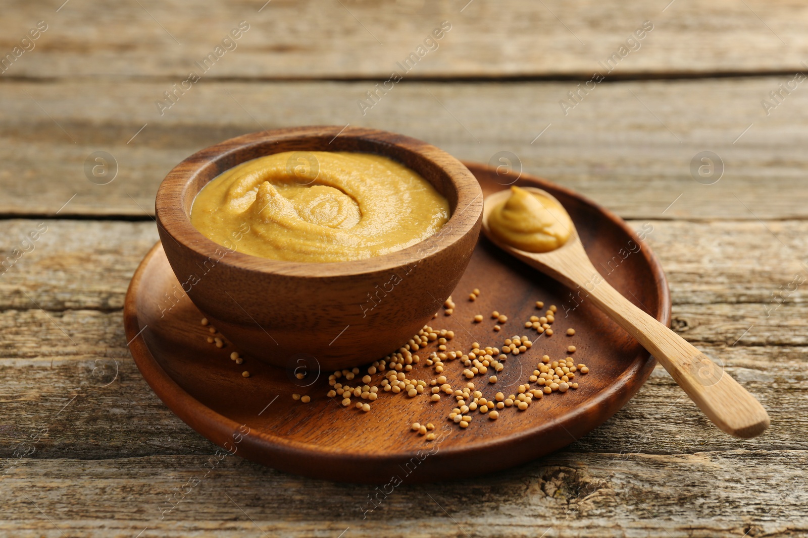 Photo of Spoon and bowl of tasty mustard sauce with dry seeds on wooden table