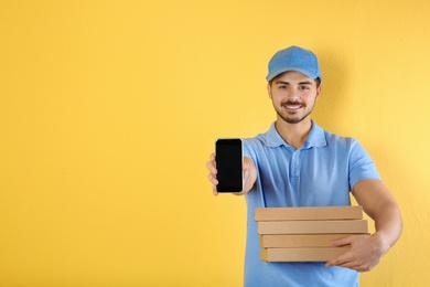 Photo of Young man holding pizza boxes and smartphone on on color background, mockup for design. Online food delivery