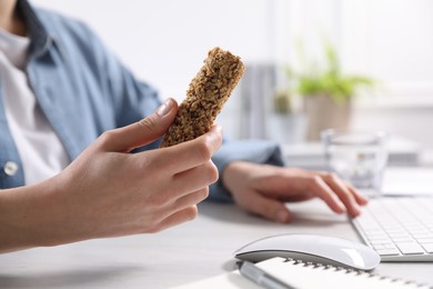 Photo of Woman holding tasty granola bar working with computer at light table in office, closeup