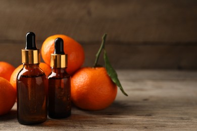 Photo of Bottles of tangerine essential oil and fresh fruits on wooden table. Space for text