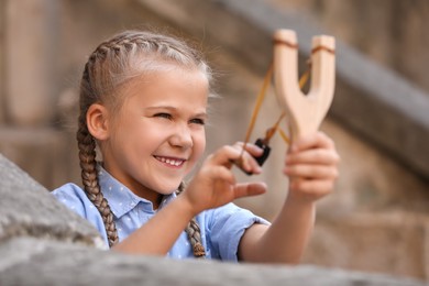 Photo of Cute little girl playing with slingshot outdoors