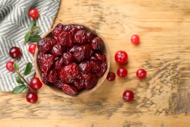 Photo of Tasty dried cranberries in bowl, fresh ones and leaves on wooden table, top view. Space for text