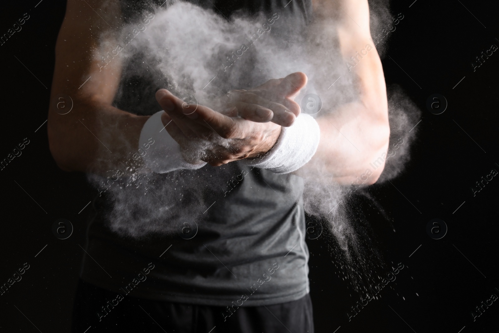 Photo of Young man applying chalk powder on hands against dark background