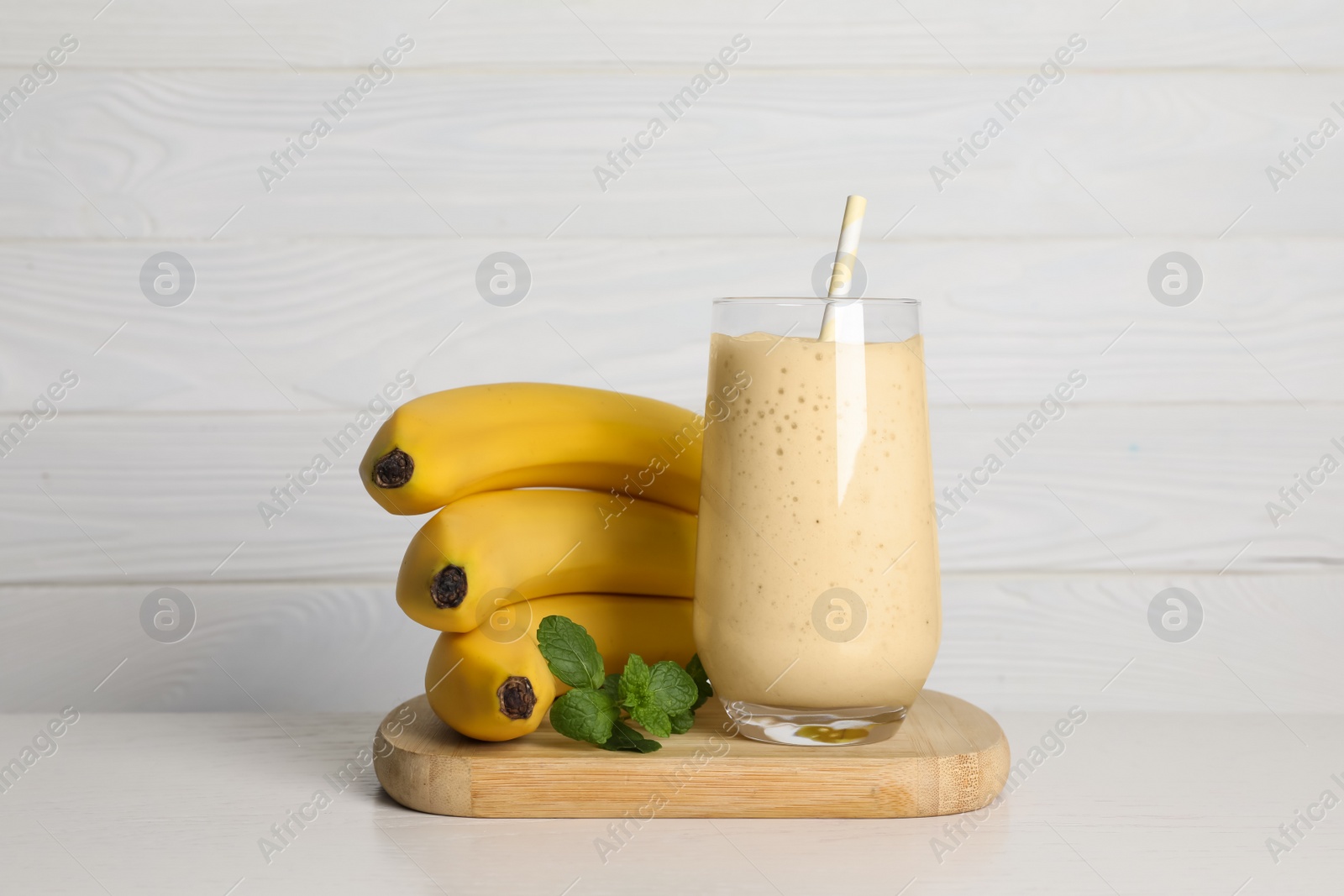 Photo of Glass of tasty smoothie, mint and fresh bananas on white wooden table