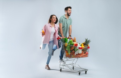 Photo of Young couple with shopping cart full of groceries on grey background