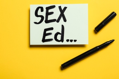 Note with text "SEX ED..." on yellow background, flat lay