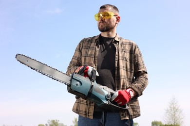 Man with modern saw against blue sky, low angle view