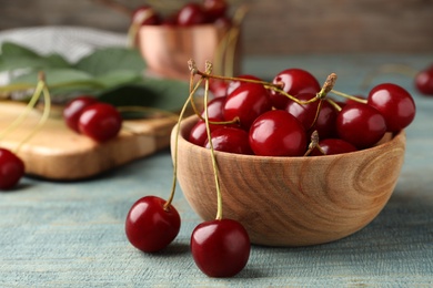 Photo of Wooden bowl of delicious cherries on blue table, closeup view. Space for text