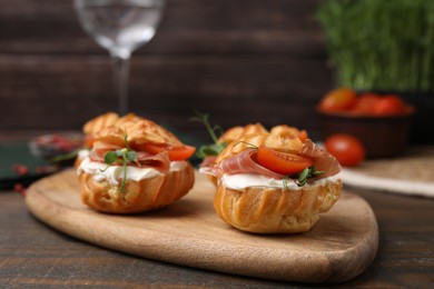 Delicious profiteroles with cream cheese, jamon and tomato on wooden table, closeup