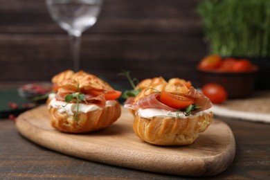 Photo of Delicious profiteroles with cream cheese, jamon and tomato on wooden table, closeup