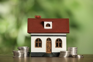 Photo of Mortgage concept. House model and coins on wooden table against blurred background, closeup