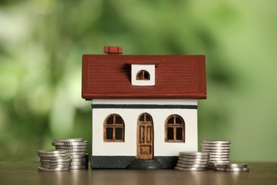 Mortgage concept. House model and coins on wooden table against blurred background, closeup