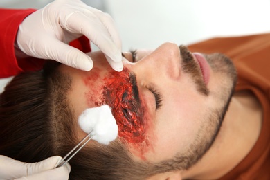 Photo of Nurse cleaning young man's head injury in clinic, closeup. First aid