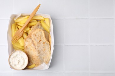 Delicious fish and chips with tasty sauce served on white tiled table, top view. Space for text