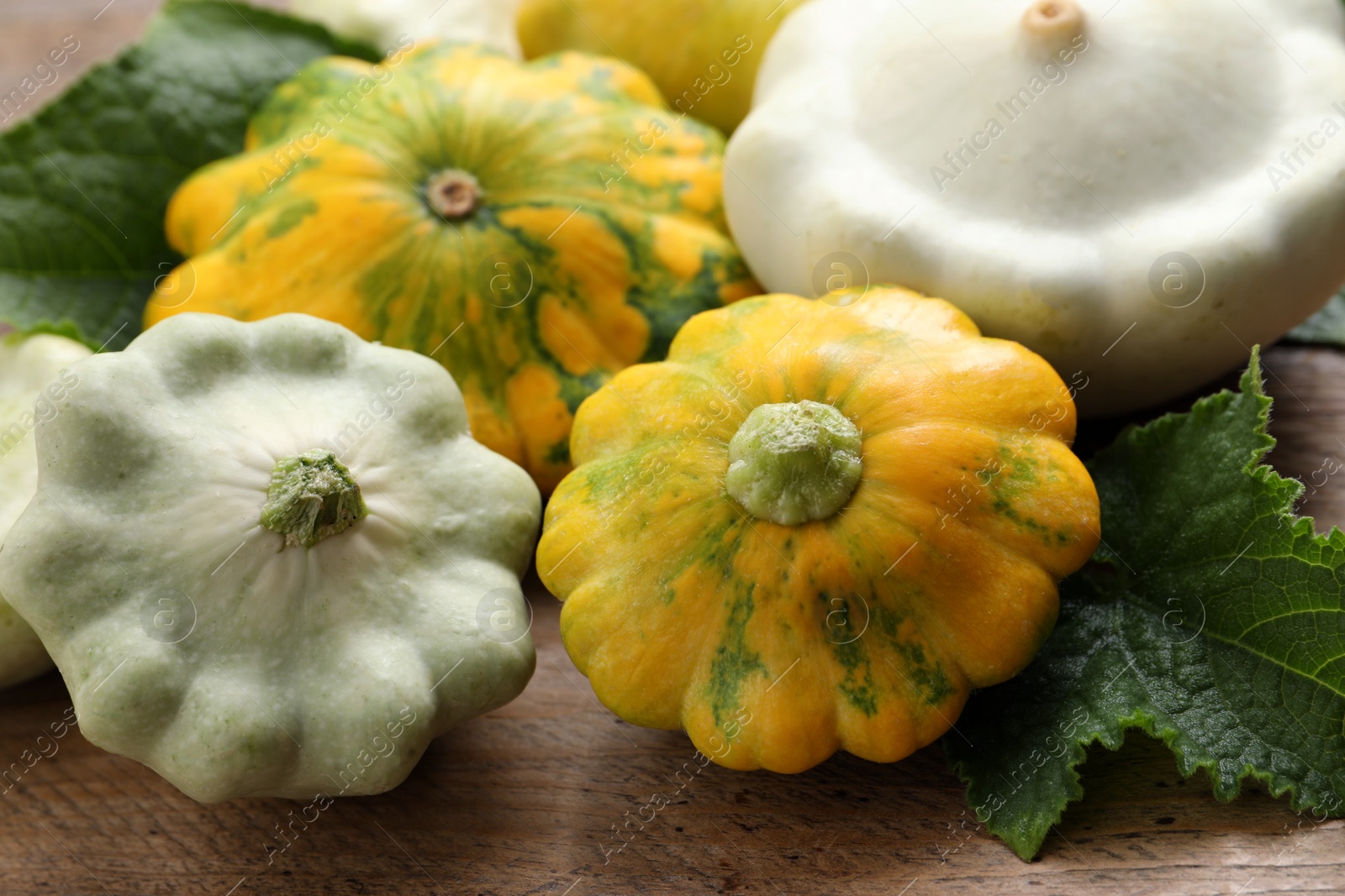 Photo of Fresh ripe pattypan squashes with leaves on wooden table, closeup