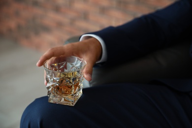 Young man with glass of whiskey indoors, closeup