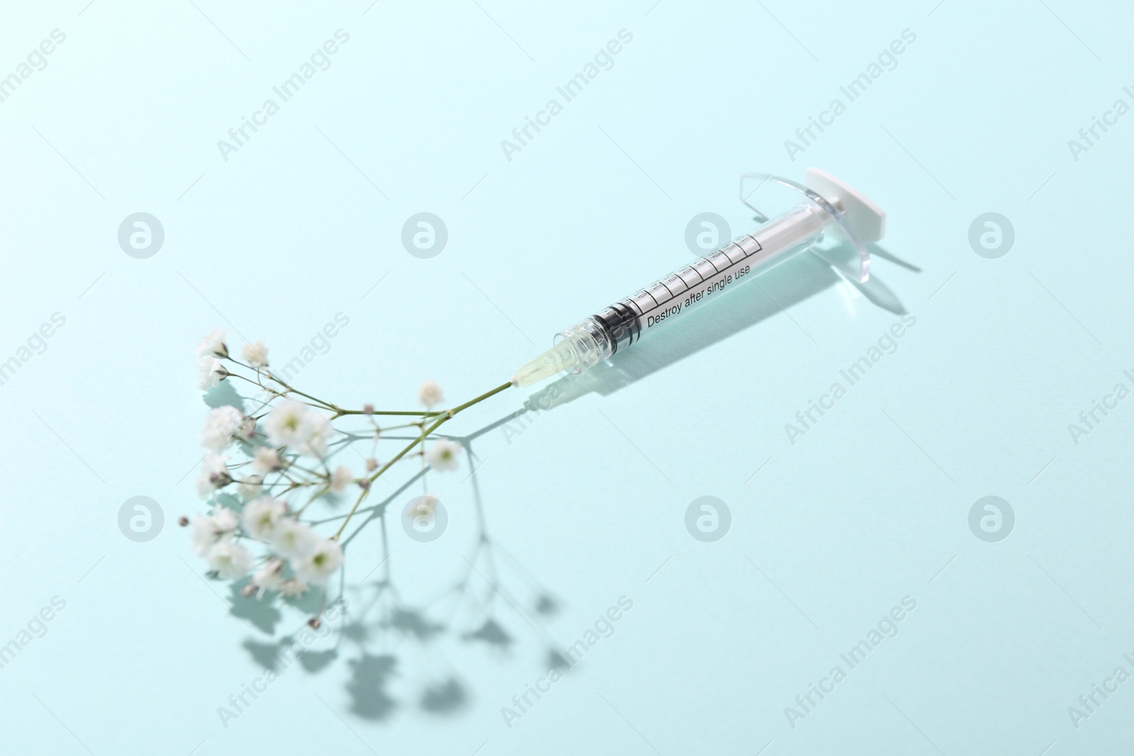 Photo of Cosmetology. Medical syringe and gypsophila on light blue background