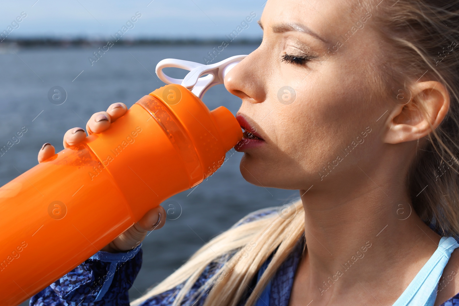 Photo of Woman in sportswear drinking protein shake near river, closeup