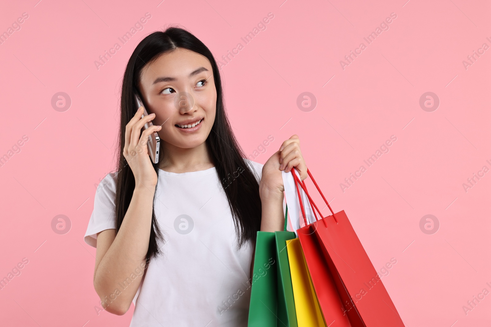 Photo of Smiling woman with shopping bags talking by smartphone on pink background. Space for text