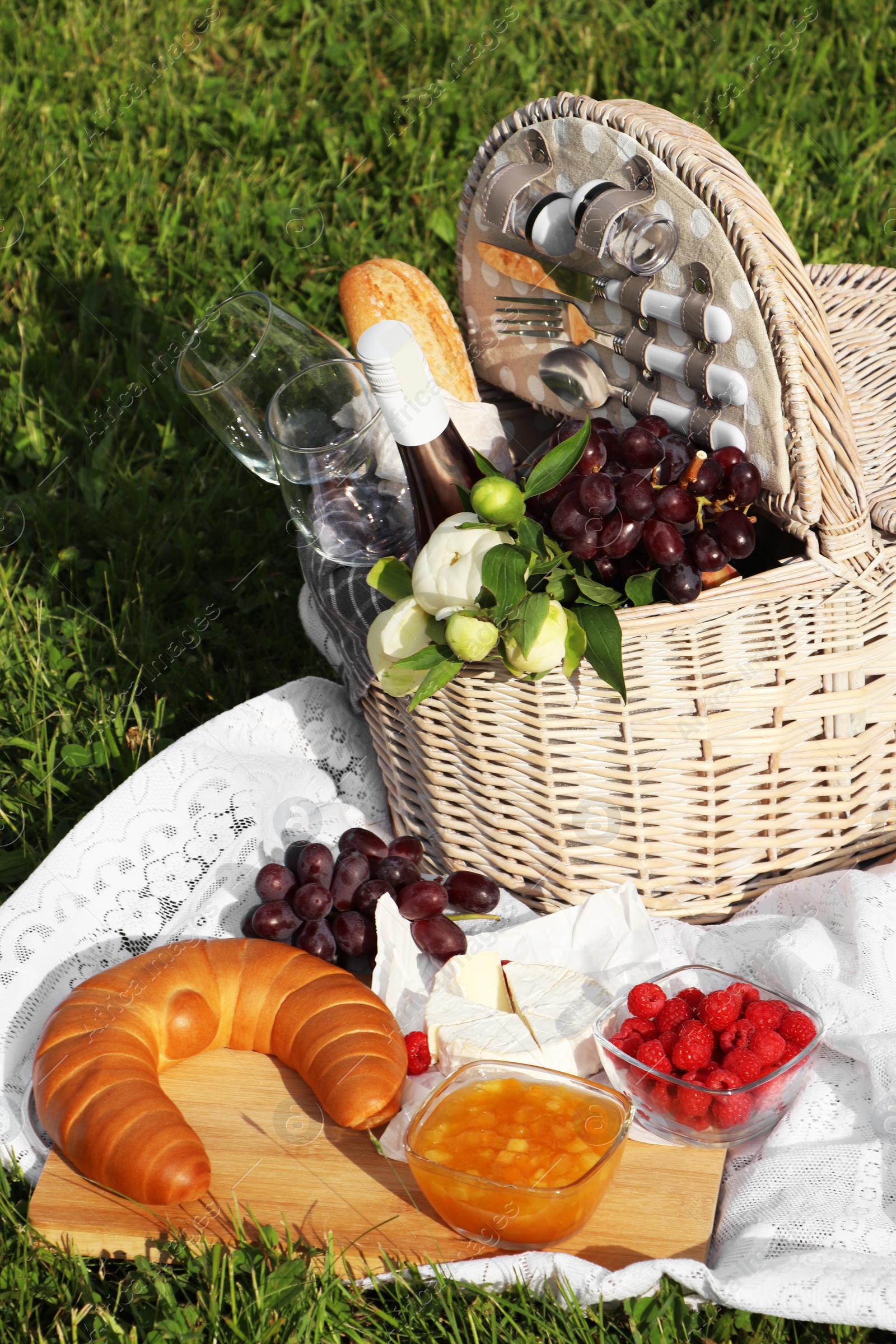 Photo of Picnic blanket with tasty food, flowers, basket and cider on green grass outdoors