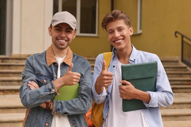 Photo of Portrait of happy young students showing thumbs up outdoors