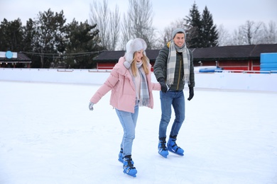Image of Happy couple skating along ice rink outdoors