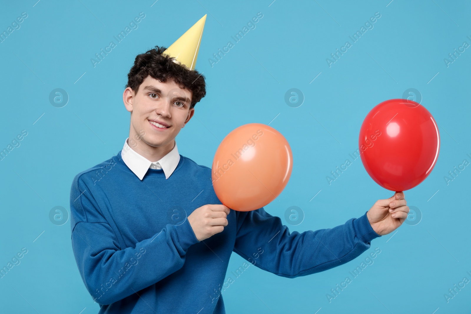 Photo of Young man in party hat with balloons on light blue background