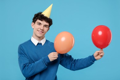 Photo of Young man in party hat with balloons on light blue background