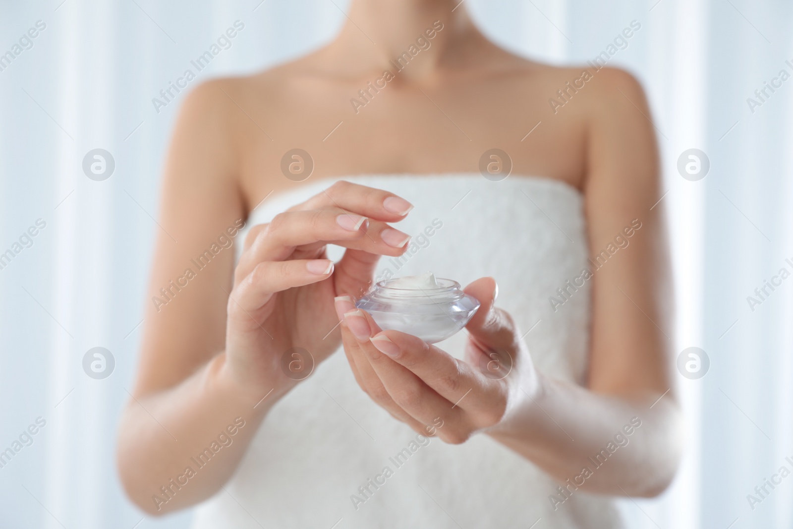 Photo of Young woman holding glass jar of cream at home, closeup