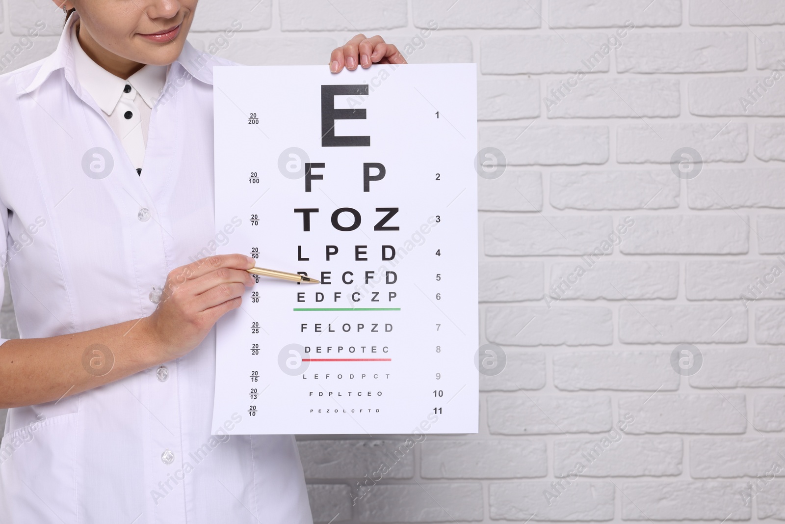 Photo of Ophthalmologist pointing at vision test chart near white brick wall, closeup. Space for text