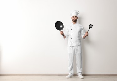 Photo of Professional chef with wok and spatula near white wall indoors. Space for text