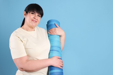 Photo of Happy overweight mature woman with yoga mat on light blue background, space for text