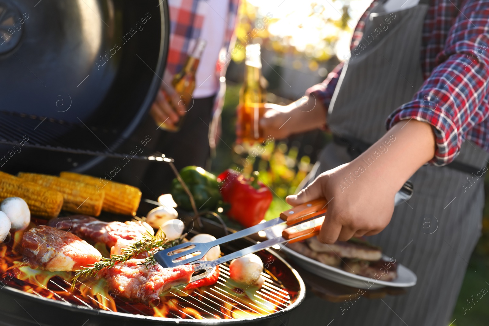 Photo of Man with drink cooking meat and vegetables on barbecue grill outdoors, closeup