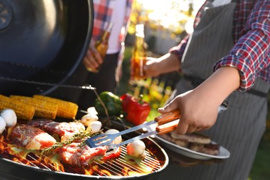 Photo of Man with drink cooking meat and vegetables on barbecue grill outdoors, closeup