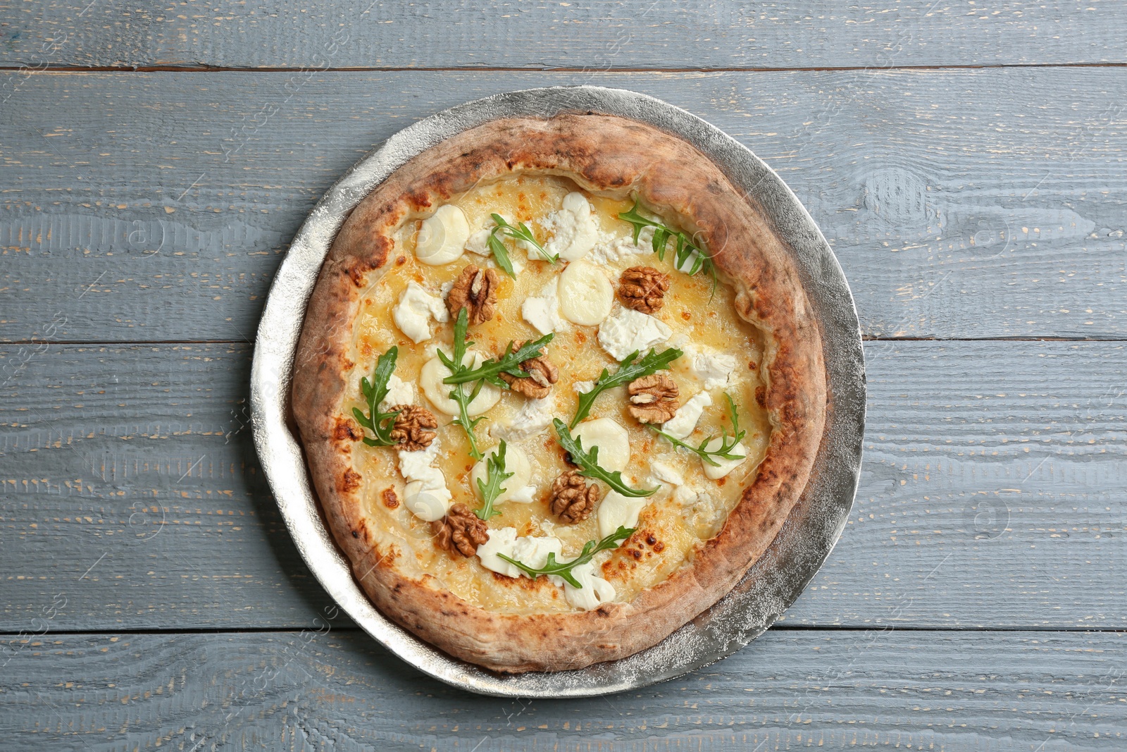 Photo of Delicious cheese pizza with walnuts and arugula on grey wooden table, top view