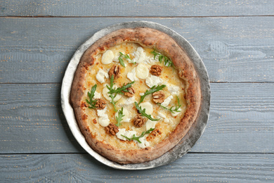 Photo of Delicious cheese pizza with walnuts and arugula on grey wooden table, top view