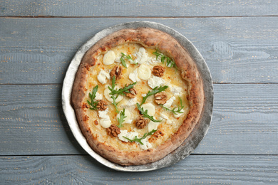 Delicious cheese pizza with walnuts and arugula on grey wooden table, top view